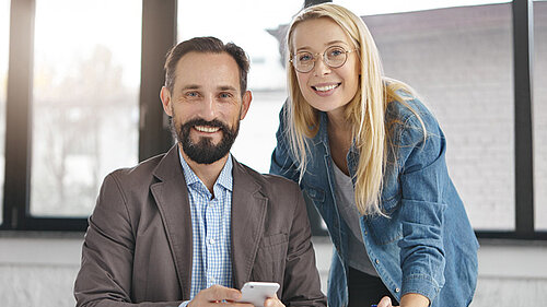 Man und Frau im Büro, lächeln in die Kamera