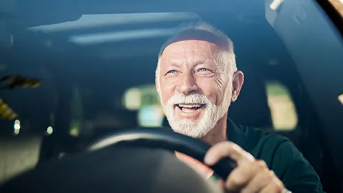 Älterer Herr sitzt hinter dem Steuer eines Autos und lächelt