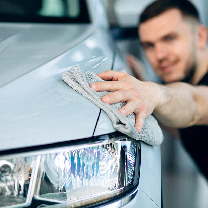 Mann säubert Motorhaube eines weißen Autos mit einem Tuch